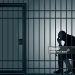 Concept of prison and arrest of an offender or criminal, with a prisoner sitting in his cell holding his head in his hands.